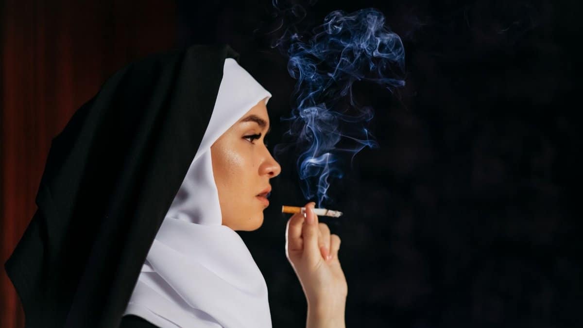 Profile of a nun in traditional habit smoking a cigarette, with smoke swirling against a dark backdrop.