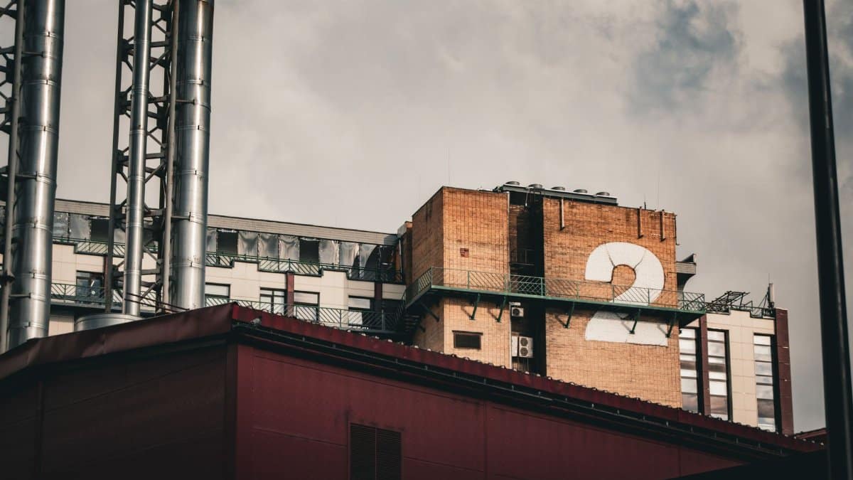 A photo featuring an industrial building roof with multiple chimneys and a number '2' sign under cloudy skies.