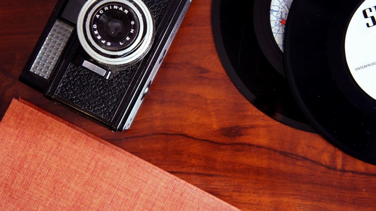 An artistic display of a vintage camera and vinyl records on a polished wooden desk.