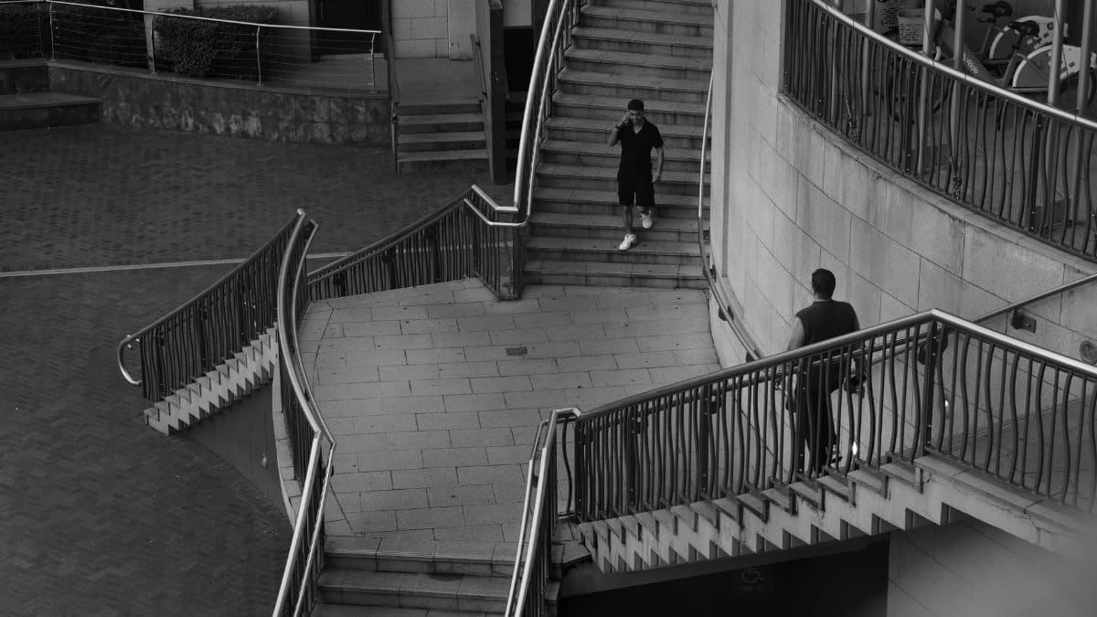Monochrome photo of two people on urban staircases, creating a geometric pattern.