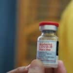 Detailed view of a Moderna COVID-19 vaccine vial held in hand, highlighting immunization efforts.