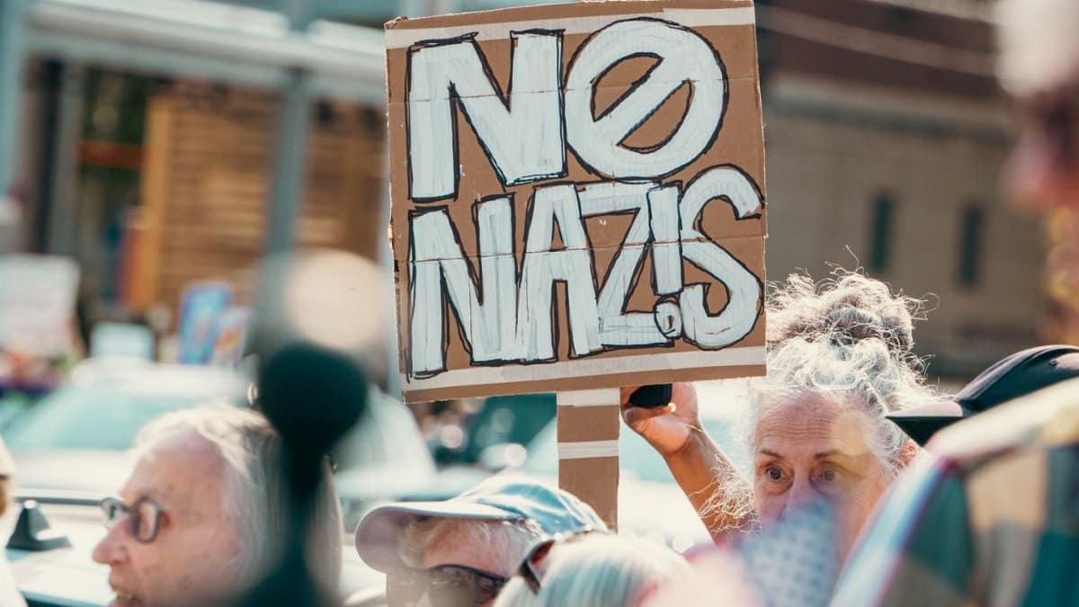 A vibrant anti-fascist protest features a crowd holding a NO NAZIS sign outdoors.