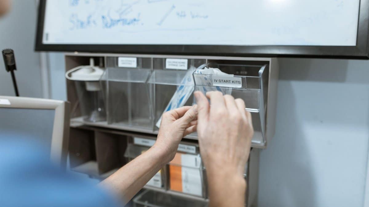A medical professional selects items from an IV start kit dispenser in a hospital setting.