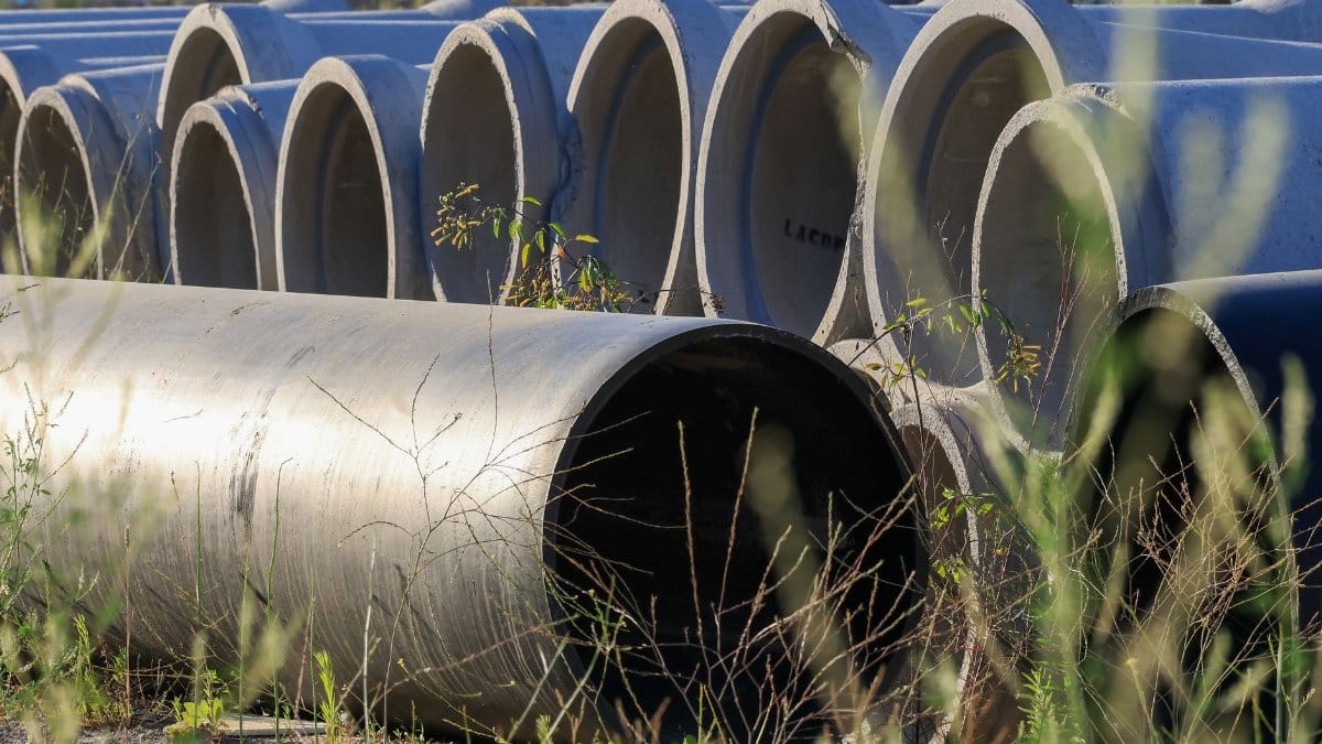Stacked concrete pipes in an outdoor storage area surrounded by grass.