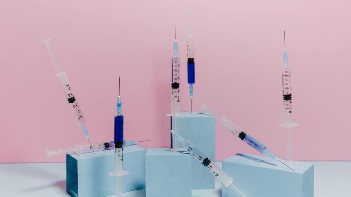A conceptual studio shot of medical syringes on a pastel pink and blue background.