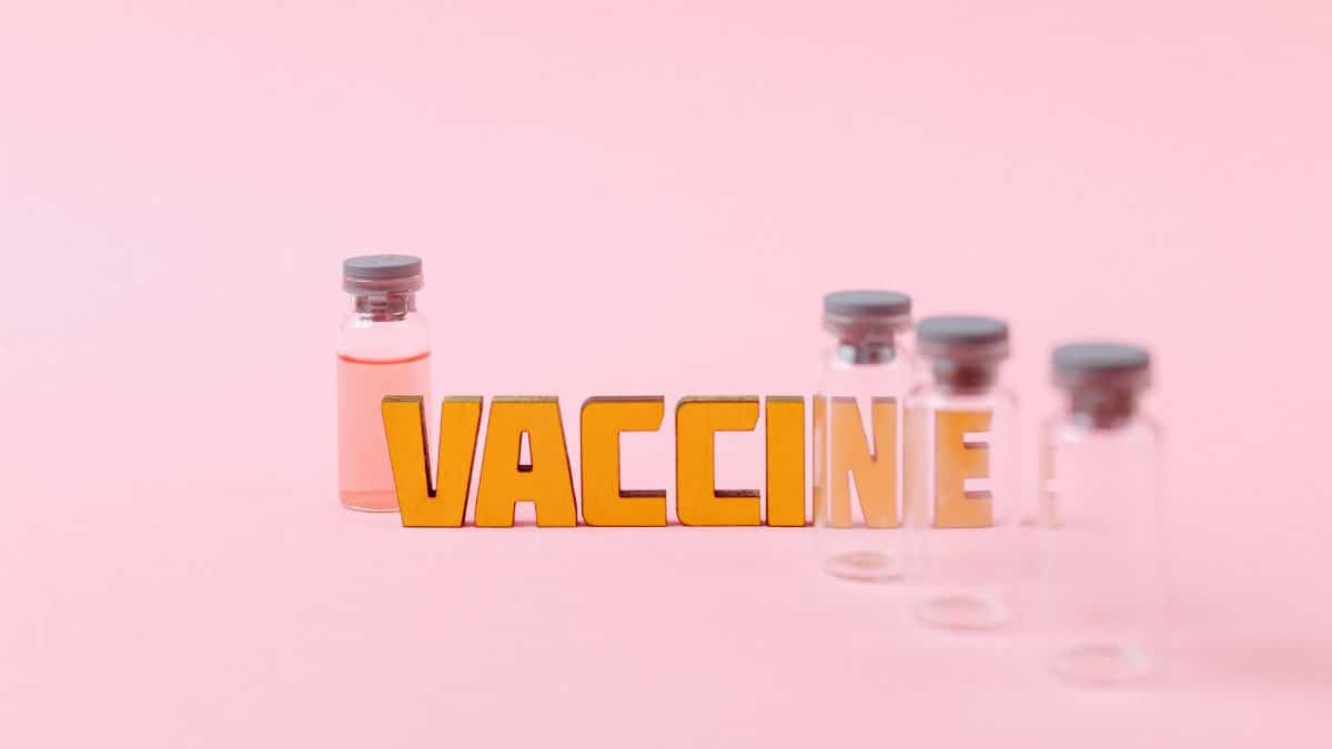 Conceptual image of vaccine vials with bold 'VACCINE' text on a pink background.