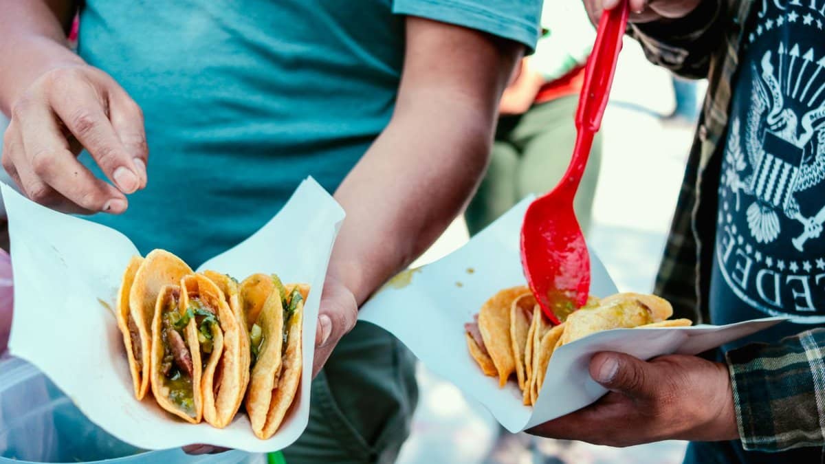 Close-up of street food vendors serving freshly-made tacos with vibrant ingredients at a market.