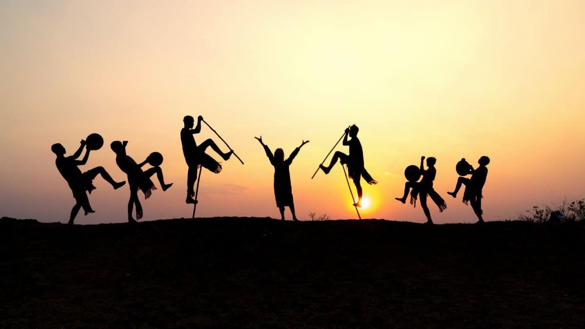 Silhouettes of dancers performing energetically against a vibrant sunset sky.