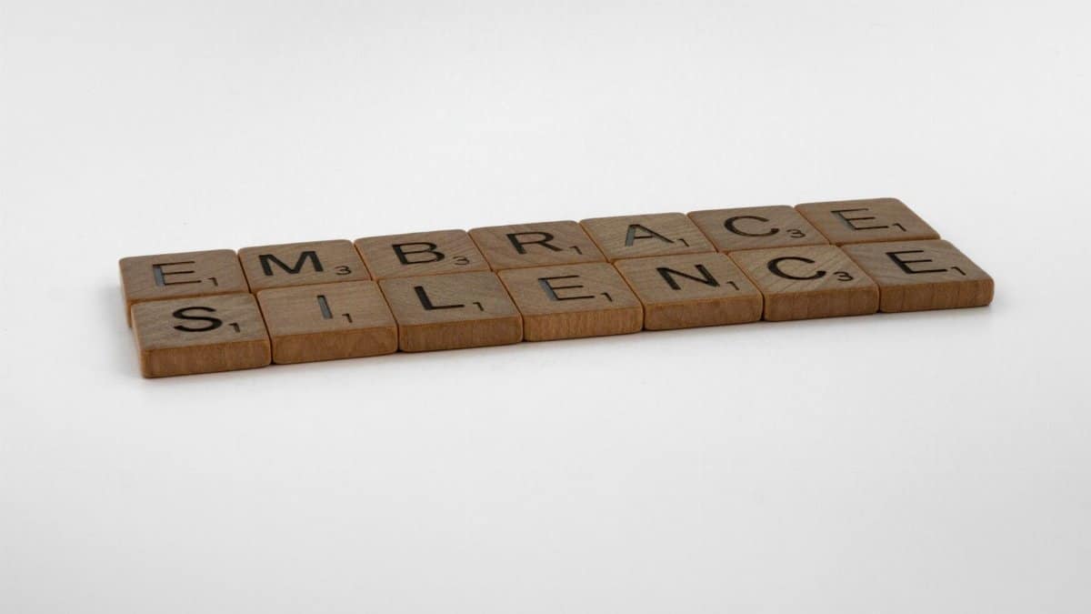 Close-up of wooden Scrabble tiles spelling 'Embrace Silence' on a white surface.