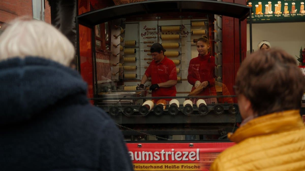 Street vendors prepare traditional Kürtőskalács at a festive market.