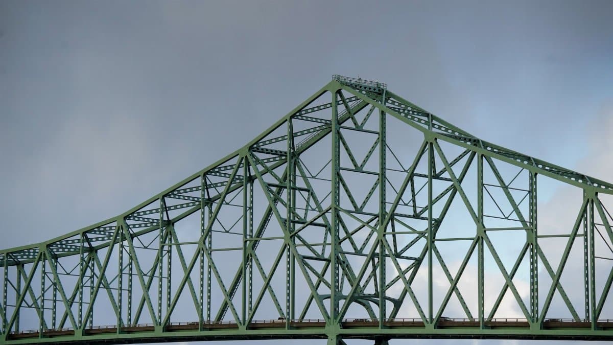 Close-up view of a green steel truss bridge against a cloudy sky, showcasing architectural design.