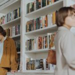 Two people browsing books in a cozy bookstore. A man checks his phone while a woman selects a book.