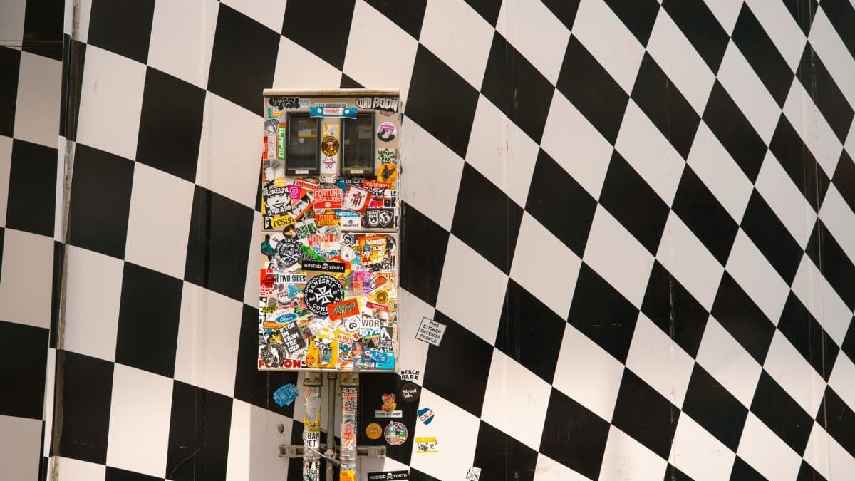 A colorful sticker-covered utility box against a black and white checkered wall in Tokyo.