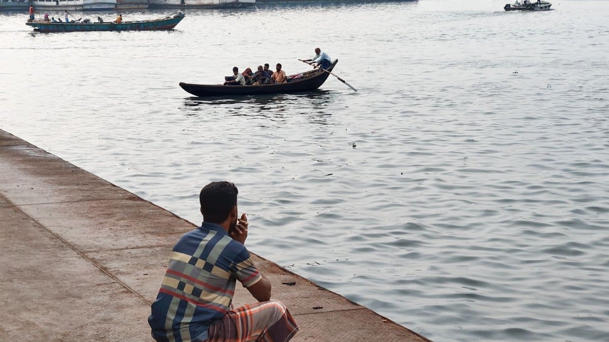 View of people in small boats on a bustling riverfront with a man sitting by the shore.