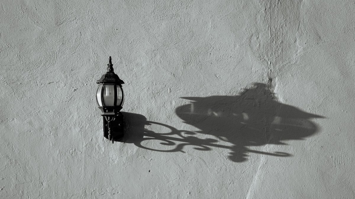 An ornate vintage lamp casts a detailed shadow on a textured wall, blending classic elegance with architectural style.