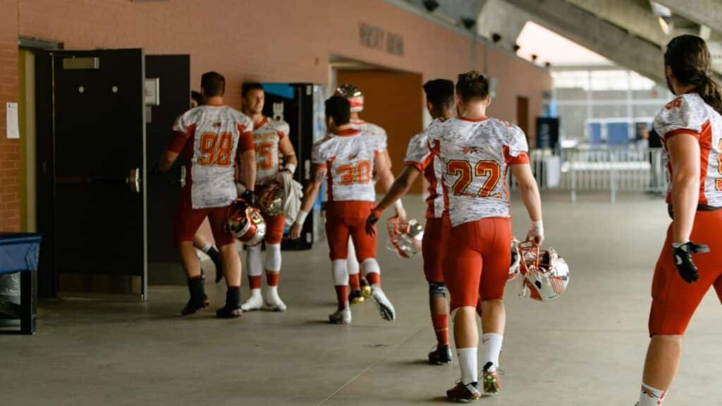 Group of football players in uniforms walking into locker room after game.