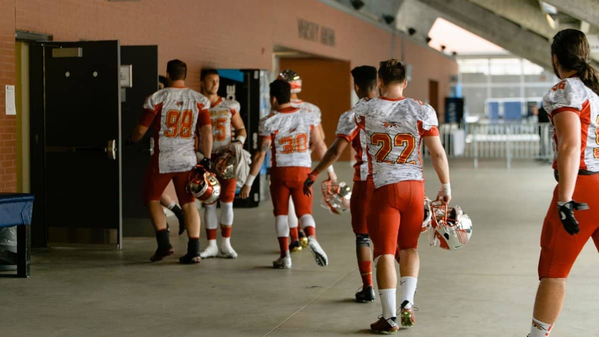 Group of football players in uniforms walking into locker room after game.