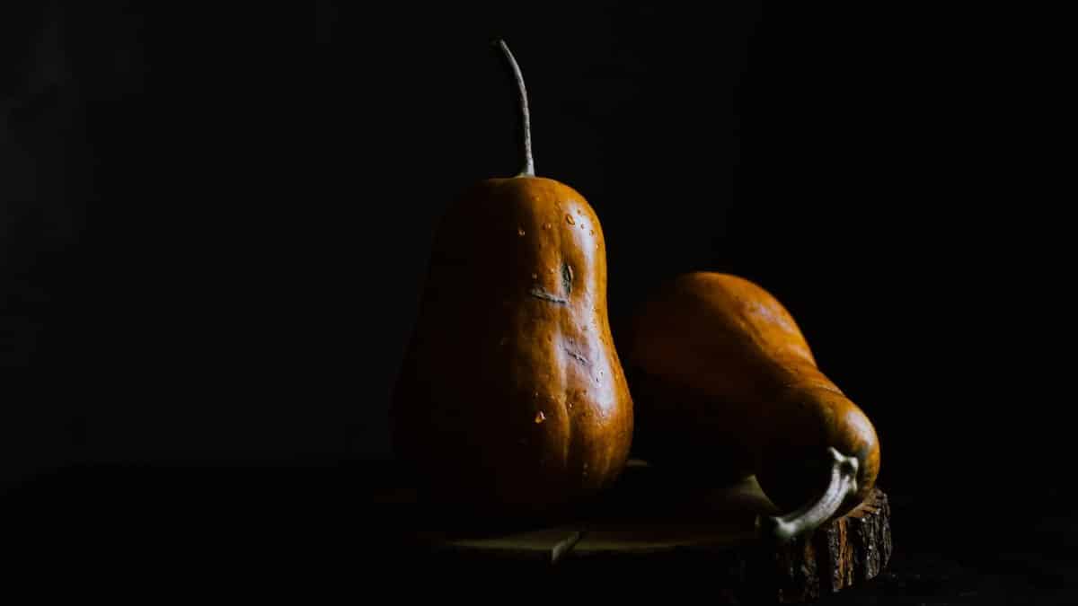 Ripe whole tear shaped pumpkins with water drops on surface placed on wooden board against black background while illuminated by light on side