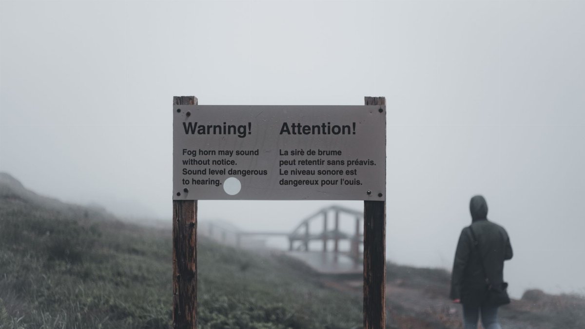 A foggy landscape with a warning sign and a lone person walking away, creating a mysterious atmosphere.