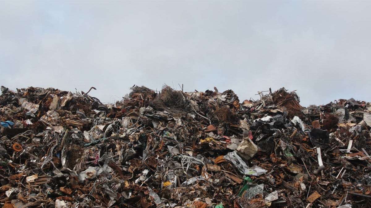 A large pile of scrap metal and waste at a landfill against a cloudy sky.