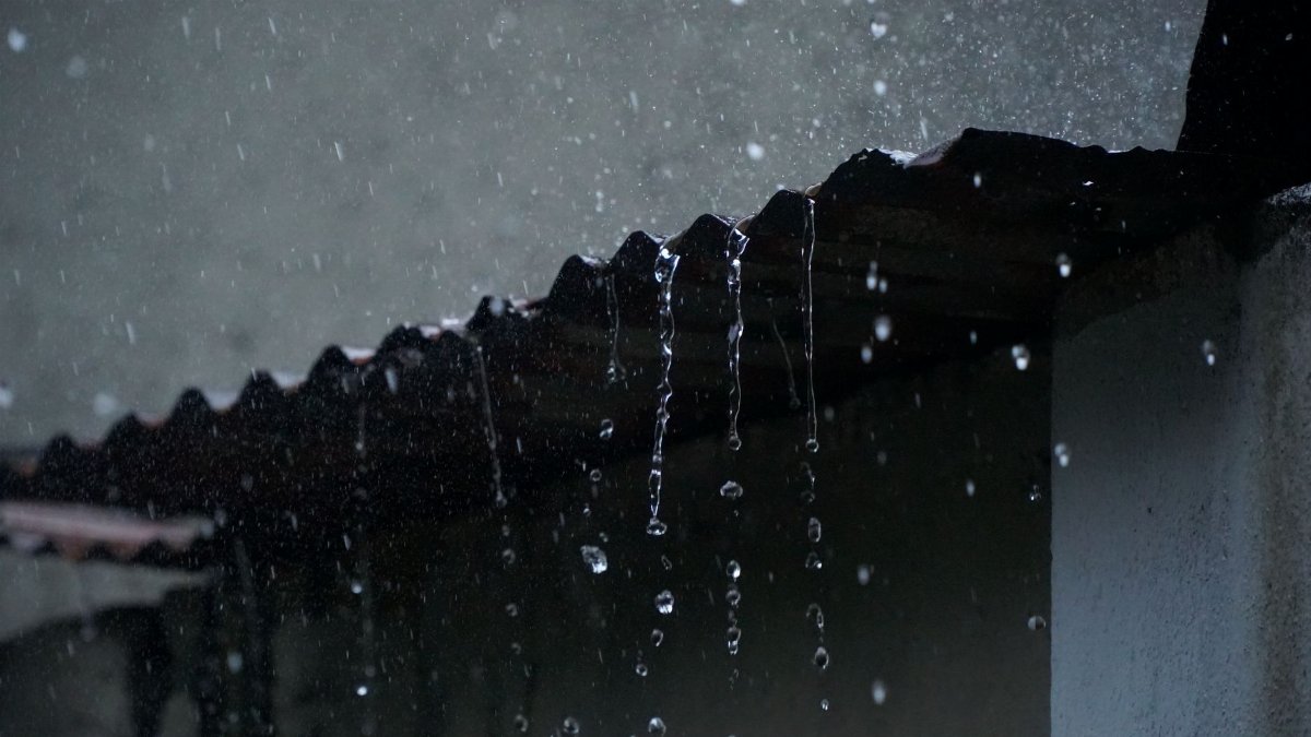 Close-up of rainwater flowing off a corrugated roof in low light, creating a serene ambiance.