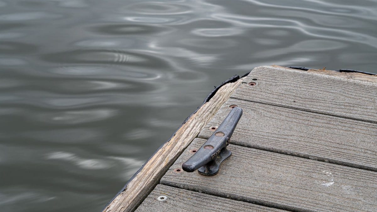 A tranquil scene of a wooden dock with a metal cleat by a rippling water surface, perfect for relaxation.