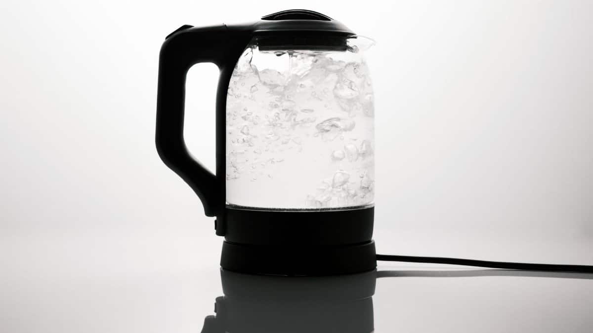 A sleek electric kettle boiling water, captured on a reflective white surface.
