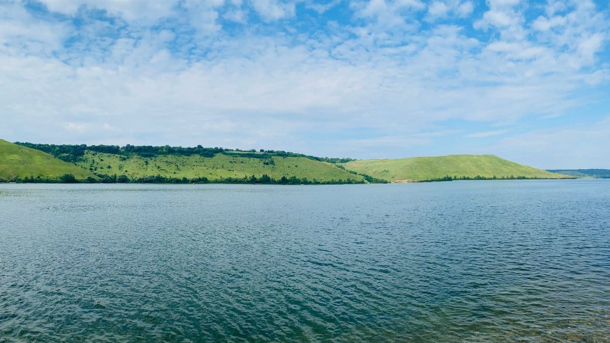 Peaceful lake with lush green hills and clear blue sky, perfect for travel and nature enthusiasts.