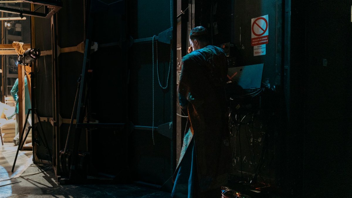 Actor stands backstage in dim lighting, ready to perform. Mysterious and artistic scene.