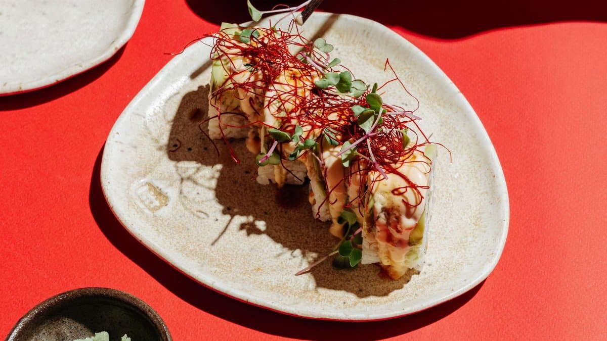Delicious sushi roll with fresh garnishes served on a ceramic plate over a red background.