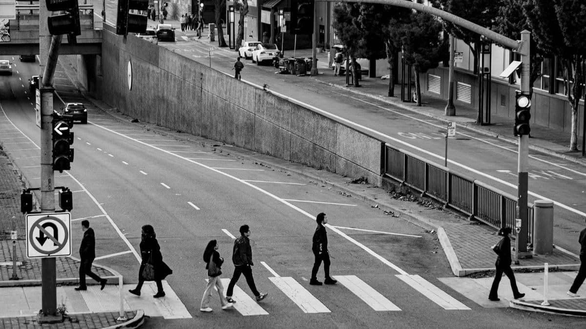 Black and white photo of people crossing a city street intersection.