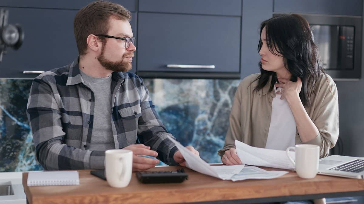 A young couple sitting at a table discussing bills and financial plans in a modern kitchen.