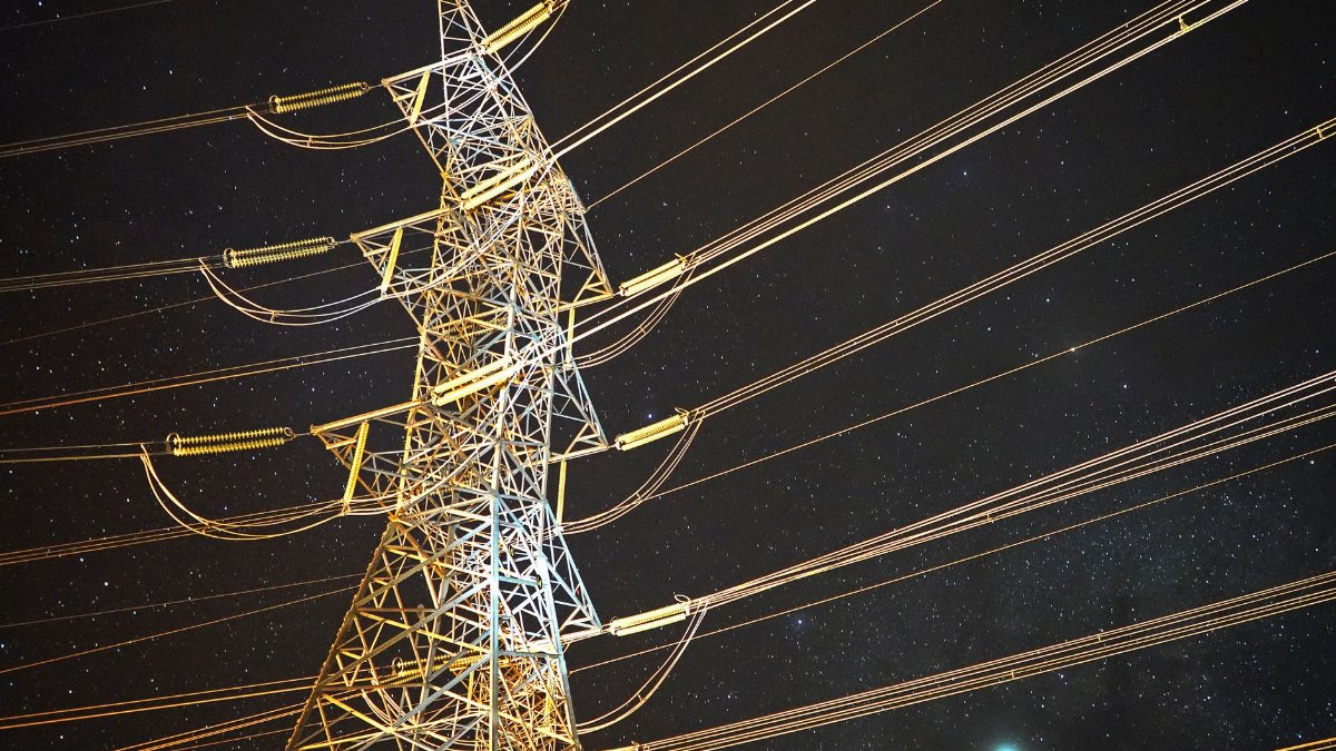 Illuminated power tower against a starry night sky, showcasing energy infrastructure.
