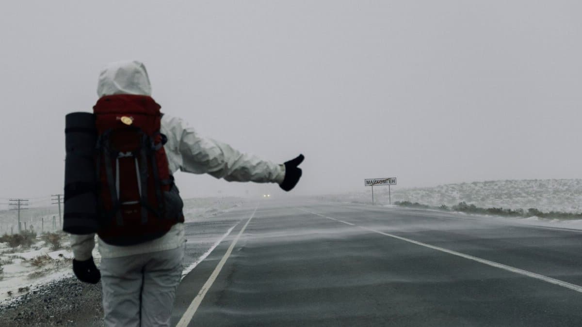 A lone traveler in a snowstorm hitchhiking on an empty highway, highlighting solitude and adventure.
