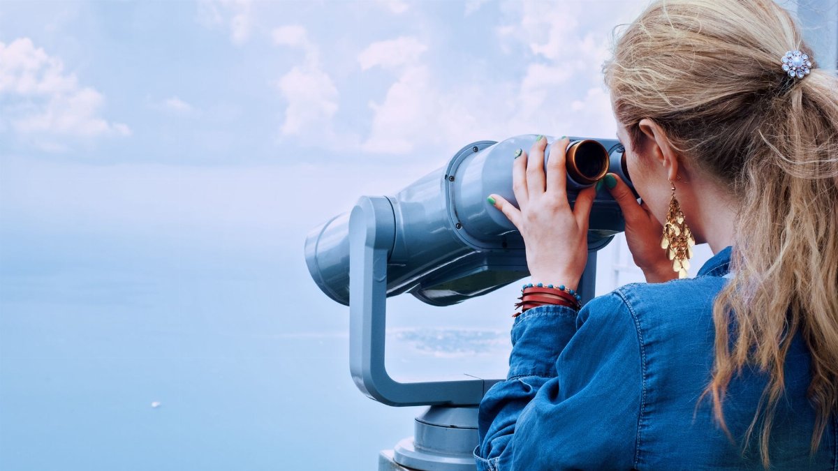 Blonde woman using a tower viewer to observe the ocean on a clear day.