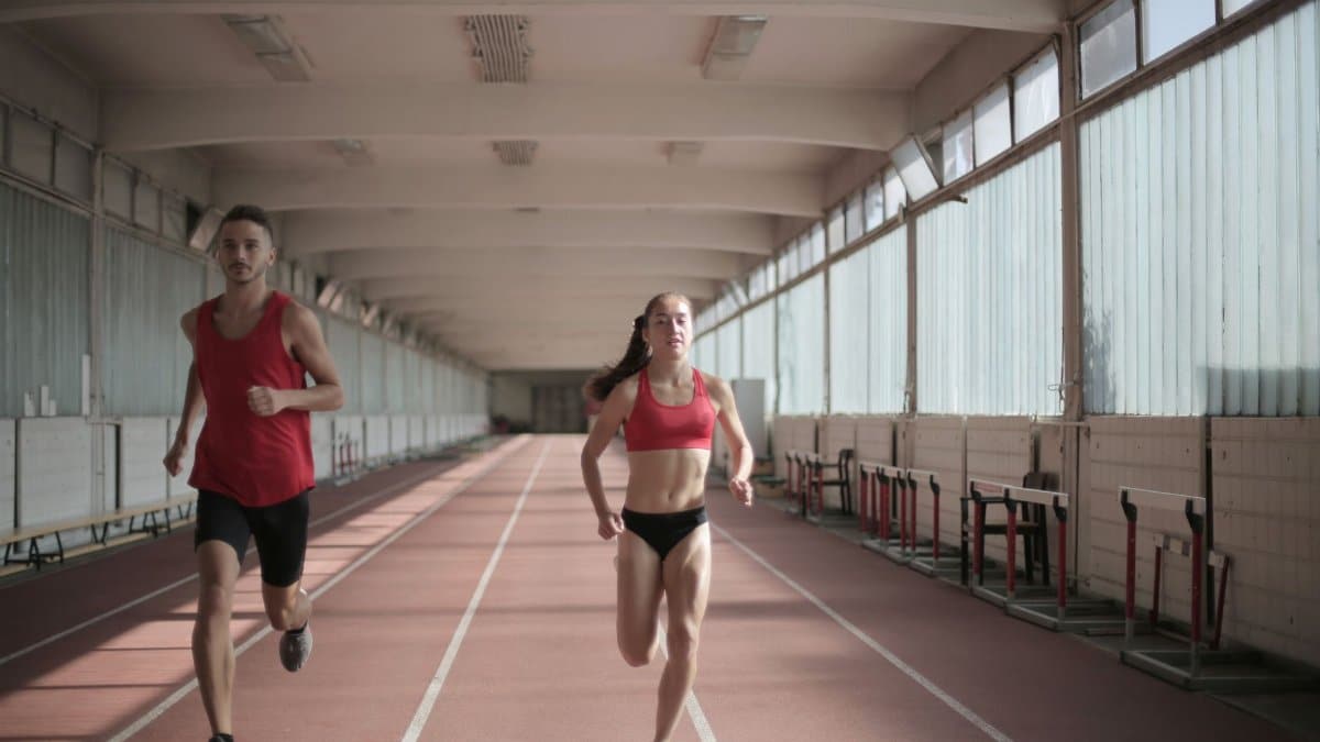 Male and female athletes running on an indoor track, showcasing fitness and energy.