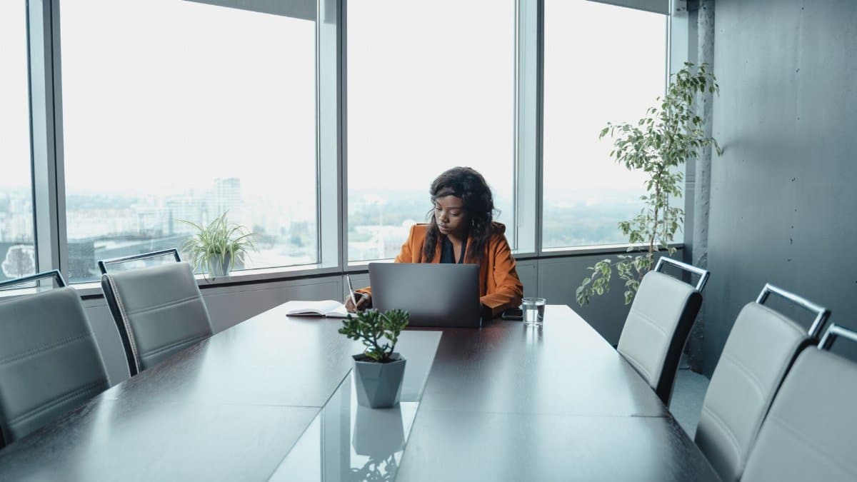African American woman working on laptop in a modern conference room with city view.