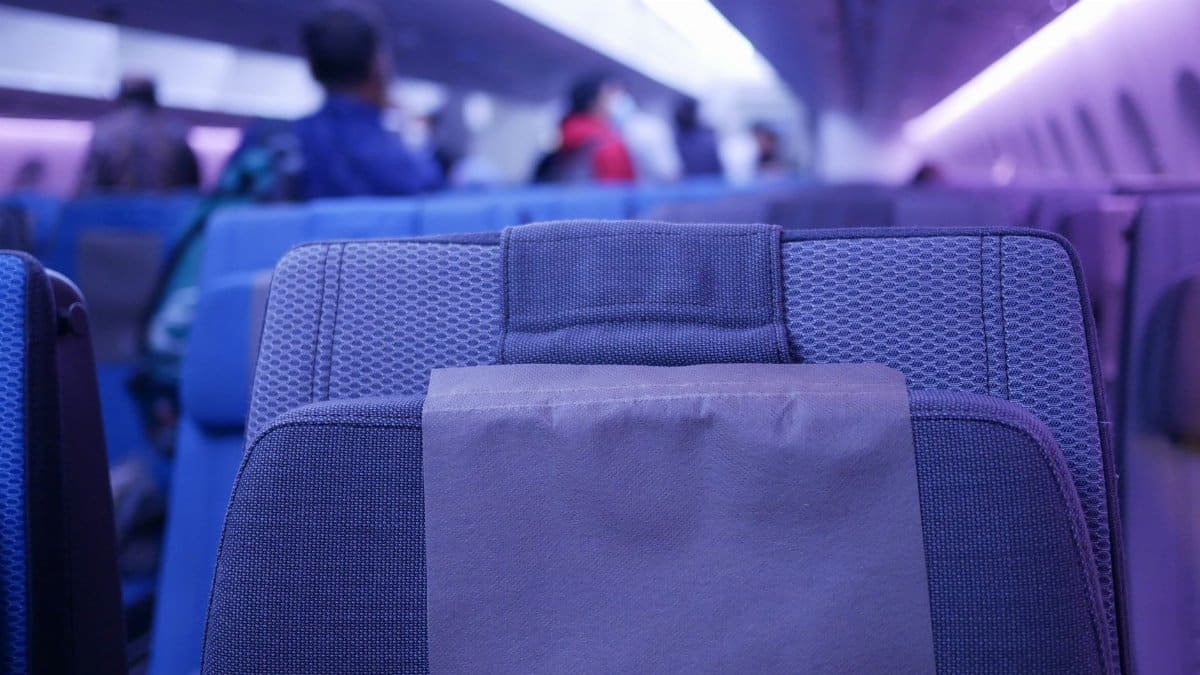 Close-up of airplane seat with blurred passengers in cabin interior lighting.