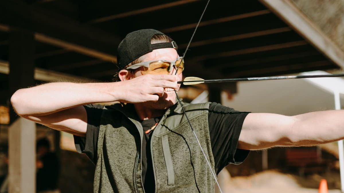 An archer concentrating as he draws his bow back, preparing to release his arrow during outdoor practice.