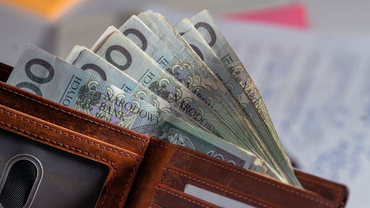 Brown leather wallet containing Polish zloty banknotes on cluttered desk