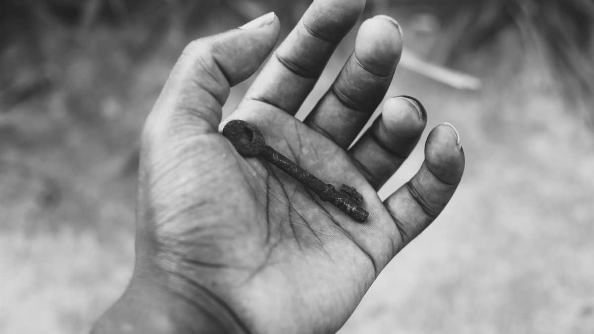 Black and white photo of a hand holding an old rusty key, creating a vintage feel.