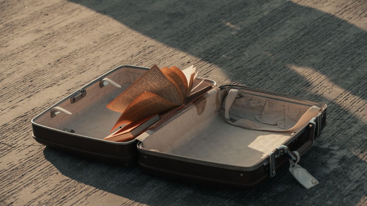An open suitcase with a book lying on a concrete surface, casting a shadow.