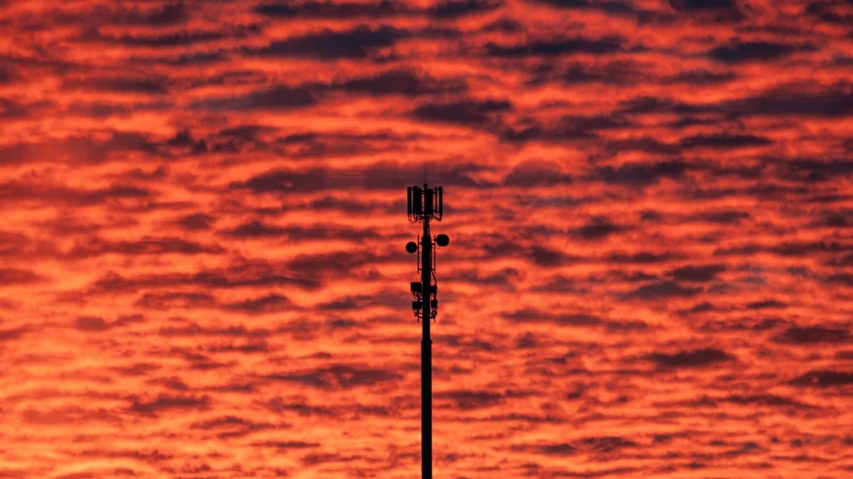 Silhouette of a communication tower against a vibrant sunset sky with dramatic cloud formations.