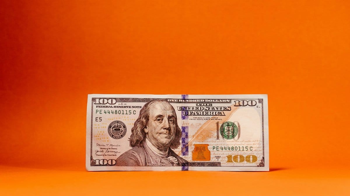 Crisp US hundred-dollar bill against a vivid orange backdrop. Ideal for finance themes.