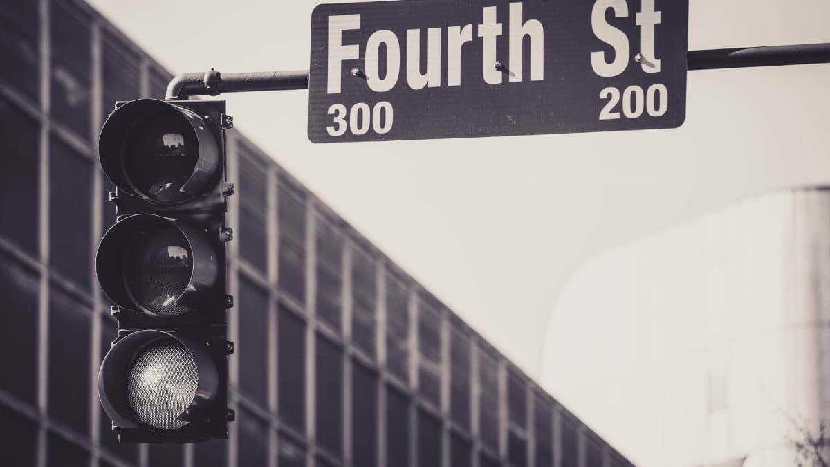 A black and white image of a traffic light and Fourth Street sign in a city environment.