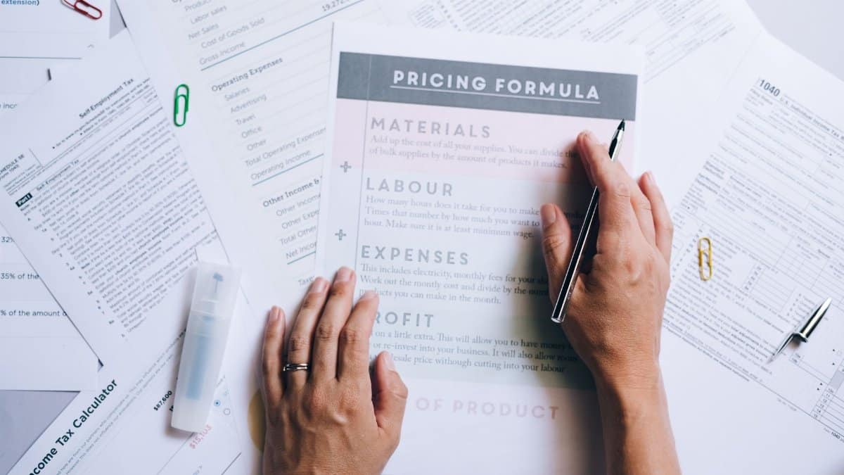 Hands organizing business documents and pricing formula papers on an office desk.