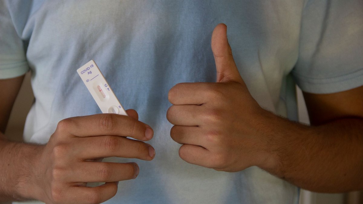 A person showing a COVID-19 antigen test and giving a thumbs up, indicating a negative result.
