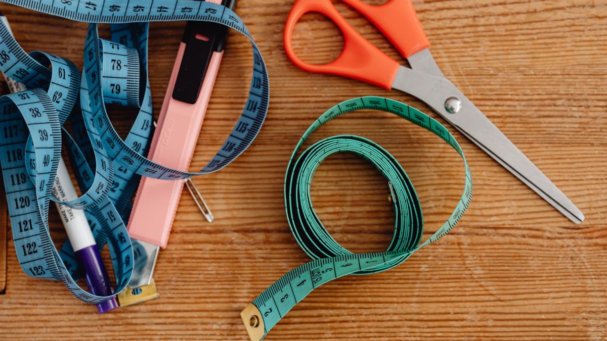 Top view of sewing tools including scissors, tape measures, and a stapler on a wooden surface.
