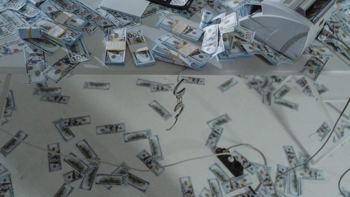 Stacks of US dollar bills scattered across a desk with a money counter and calculator.