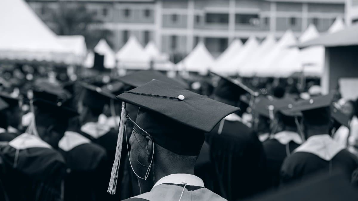 A black and white photo of students in caps and gowns at a university graduation ceremony outdoors.